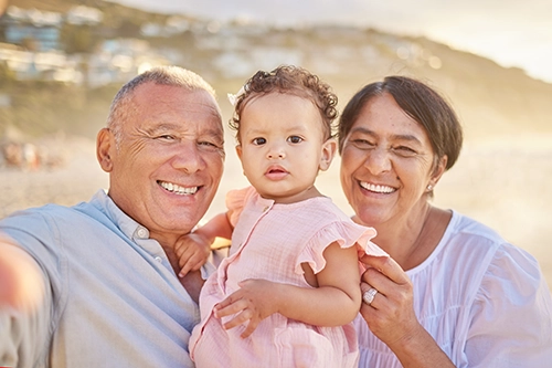 Grandparents pose for a photo with their toddler granddaughter between them on the beach - posted for life insurance as one of Tune Medicare's specialty insurance plans