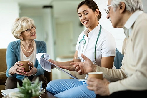 a healthcare worker sitting with a senior couple going over medicare paperwork on a clipboard